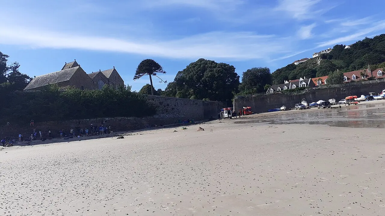 Sand at St Brelade’s Bay with the seaside church and trees behind the shore.
